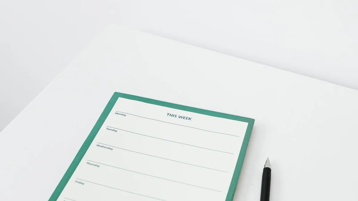 A clean and minimalist weekly planner with a pen on a white desk, perfect for organizing your schedule efficiently.