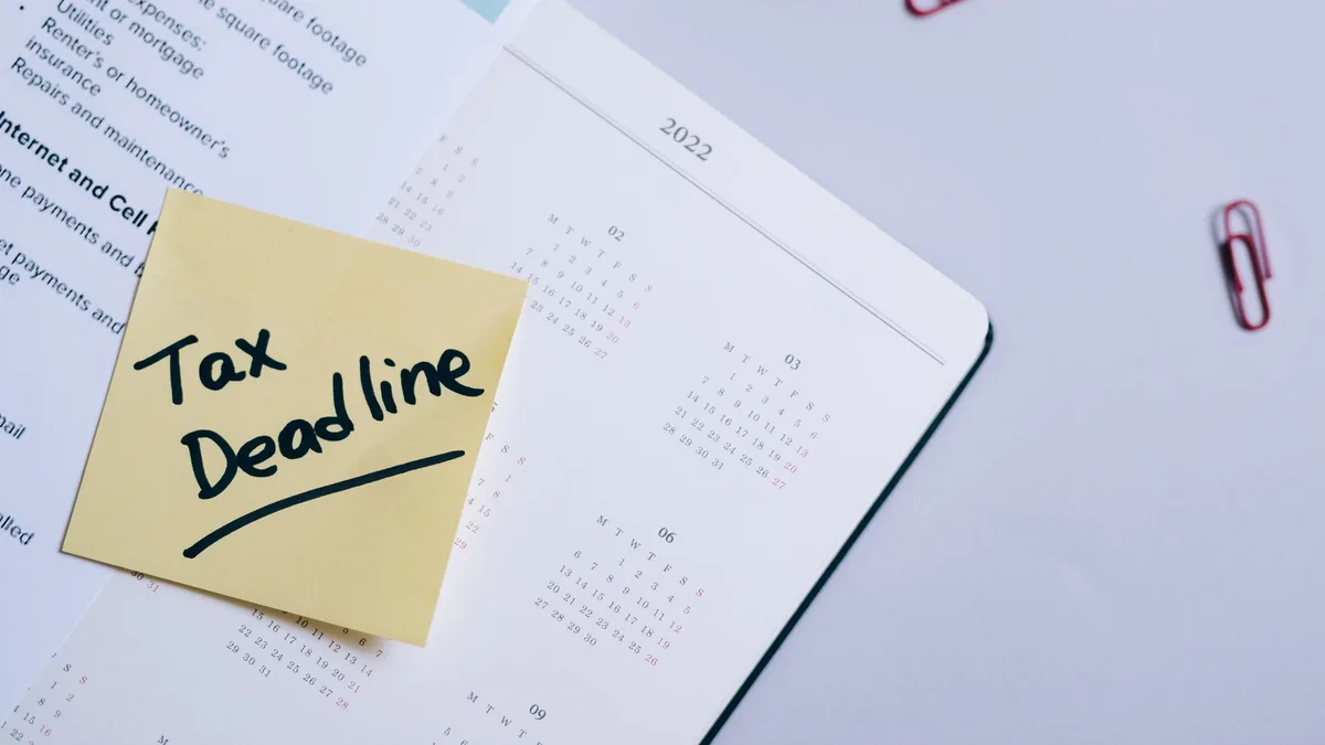 A sticky note highlights tax deadline on a calendar alongside documents, emphasizing financial planning.