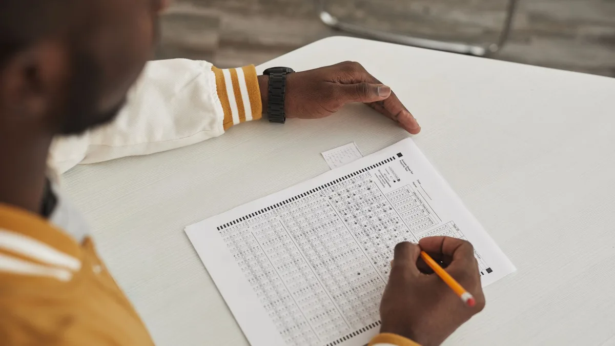 Focused student marking answers on a multiple choice exam sheet in a classroom setting.