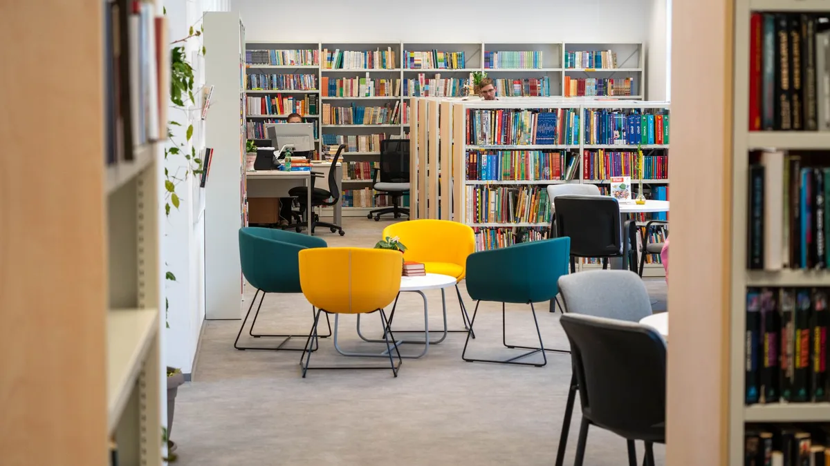 Bright library space featuring bookshelves, colorful chairs, and desks, ideal for studying and reading.